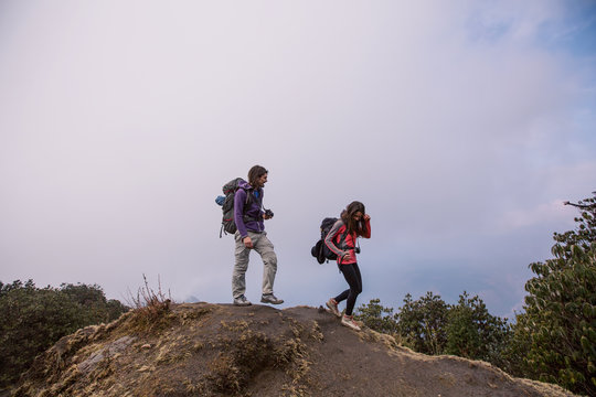 Hikers couple with backpacks walking on top of mountain and enjoying view of valley above clouds