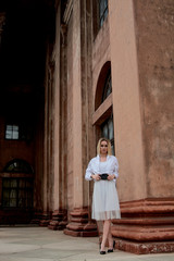 Fashion look's woman. Young woman modern portrait. Young woman dressed in white skirt and shirt posing near the old looking soviet union's architectural building with large pillars and bas-reliefs.