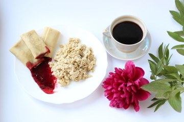 breakfast of oatmeal and pancakes with berries and a cup of coffee and next to a peony flower