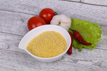 Raw couscous in the bowl served salad leaves, tomato and pepper