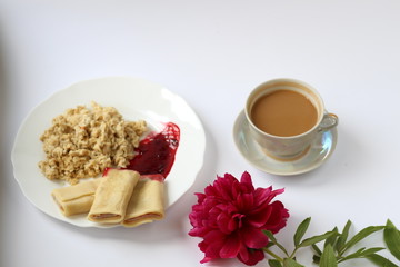 breakfast of oatmeal and pancakes with berries and a cup of coffee and next to a peony flower