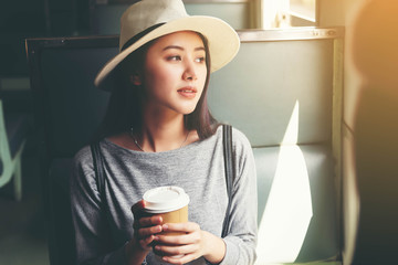 Beautiful Asian women wearing hat holding a cup of hot coffee sitting in train.