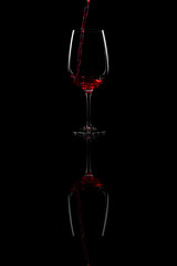 Red wine pouring into a wine glass with reflection, over black background,