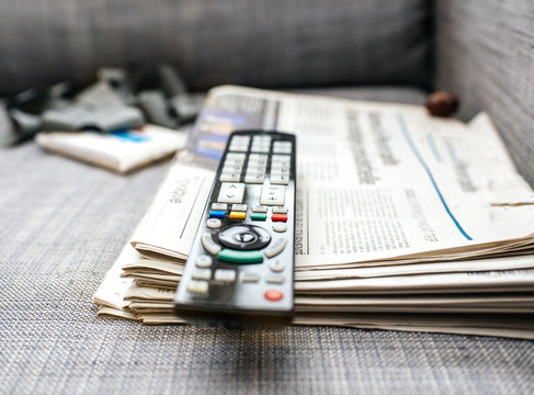 Defocused View Of Black Remote Control On Top Of Stack With Multiple Newspaper 