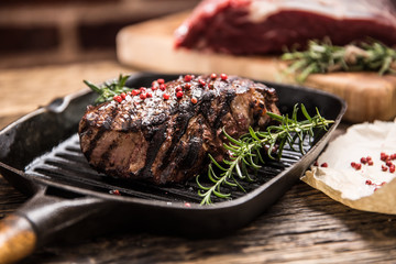 Grilled beef steak in grill pan with herbs rosemary on wooden table