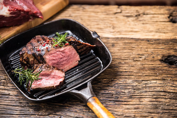 Grilled beef steak in grill pan with herbs rosemary on wooden table