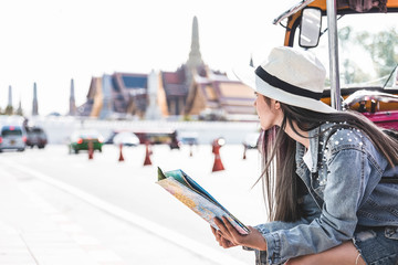 Young Asian women sitting in local taxi holing a map with Grand Palace as a blurred background, Bangkok Thailand.