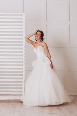 Fototapeta na wymiar Young beautiful bride in a luxurious wedding dress in the studio on white background
