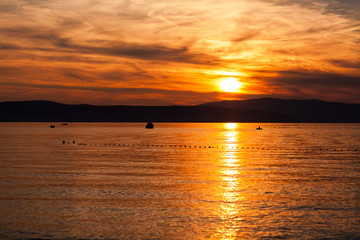 Orange sunset on the sea with the sun, a beautiful sky on the background of mountains