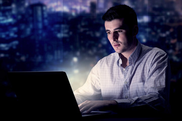 Young handsome businessman working late at night in the office with blue lights in the background