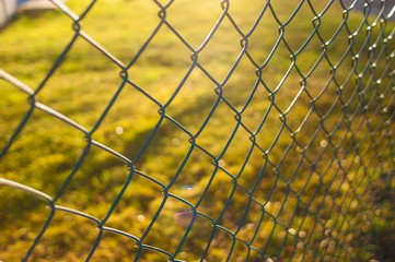 A chain link fence in front of a grass lawn.