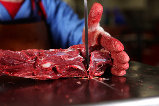 A slaughterhouse worker cuts chunks of meat into portions. Macro photo of a raw piece of meat. Hands out of focus. Professional equipment for cutting meat. Persons employee is not visible.