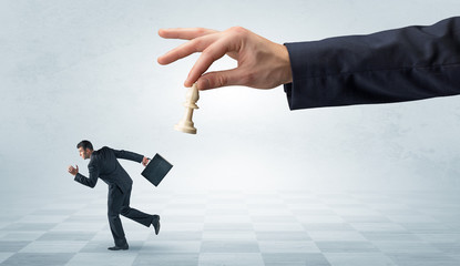 Fototapeta premium Small frail businessman with suitcase running away from big hand with chessman concept 