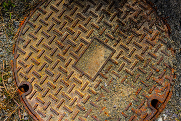 Rusty manhole cover in the middle of a pebble road.