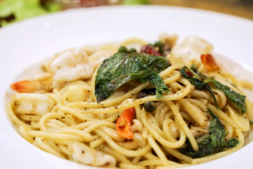 Closeup seafood stir fried spicy spaghetti in white ceramic plate on wooden table in the restaurant.