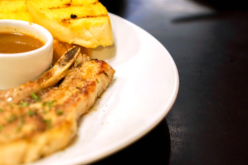 Closeup and crop t-bone pork steak and garlic bread with pepper sauce on white ceramic plate on black table in the restaurant.