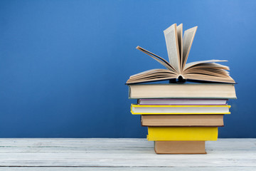 Book stacking. Open book, hardback books on wooden table and blue background. Back to school. Copy space for text.