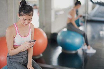 Closeup the young asian woman are playing smart phone which sitting on the fitness balls in gym near big mirror. Woman looking and searching at the phone in fitness room.