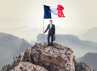 Successful businessman on the top of a mountain holding France victory flag
