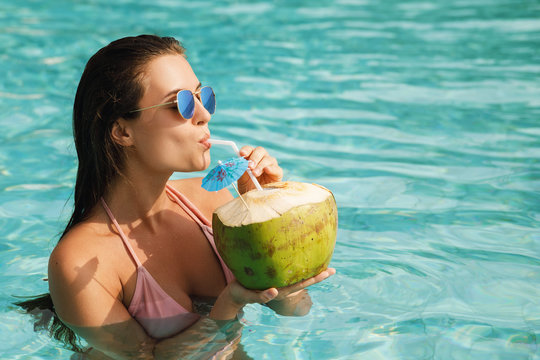 Woman relaxing in the swimming pool and drinking coconut water