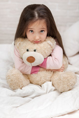 adorable little child girl hugging teddy bear in bed in morning.