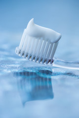 Transparent plastic toothbrush with white toothpaste on a blue white background with reflection on the glass.