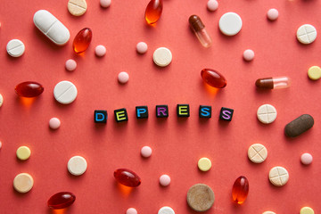 Multicolored title DEPRESS from black cubes on the table with tablets on coral background