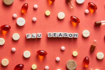 Black and white title FLU SEASON from white cubes on the table with tablets on coral background
