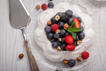 Pavlova cake with fresh summer berries and hazelnuts on glass standcake.