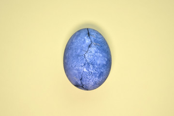 Blue egg with crack, painted in tea hibiscus, on yellow background, similar to planet and marble with copyspace