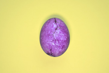 Purple egg with crack, painted in tea hibiscus, on yellow background, similar to planet and marble with copyspace