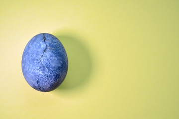 Blue egg with crack and shadow, painted in hibiscus, on yellow background, similar to planet and marble