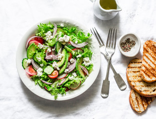 Vegetarian avocado, vegetables, feta cheese salad and grilled bread - delicious healthy lunch, snack on a light background, top view