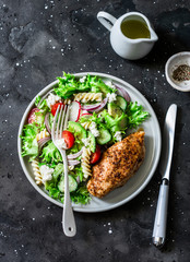 Mediterranean avocado pasta salad and baked chicken breast - healthy balanced lunch on a dark background, top view