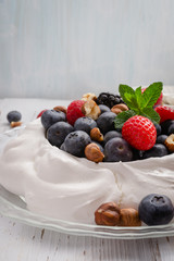 Pavlova cake with fresh summer berries and hazelnuts on glass plate.