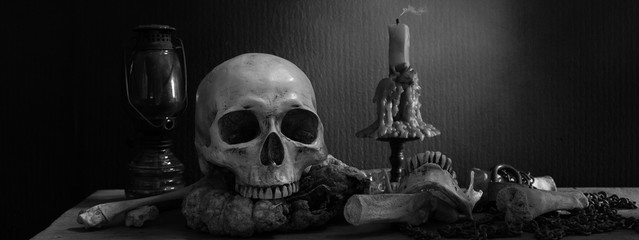 Skull on rotten pumpkin with candle light and lantern on the plank and  pile of bones