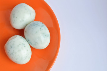 Three peeled eggs after painting in hibiscus tea, look like spoiled and covered with mold on orange plate with copyspace