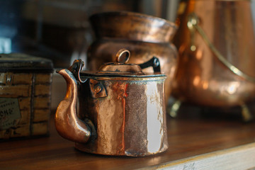 Old copper teapot stands on the background of old copper utensils