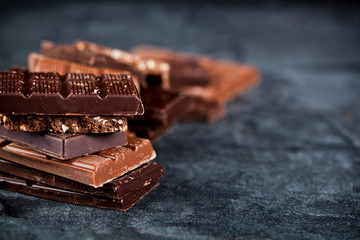 Chunks of broken chocolate stacked on black board. Chocolate bars pieces stack on black background.