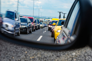 Traffic jam on European highway with big city in a background - lots of cars standing in the queue seen from the rearview mirror
