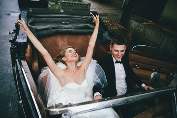 Happy stylish newlywed couple posing in a retro car