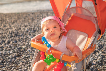 Little girl in a stroller by the sea. In a headdress.