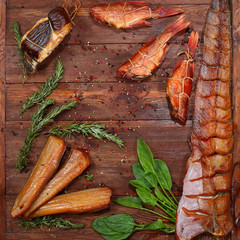 Whole smoked fish and pieces on a brown wooden background. Rosemary and spinach close up on wooden background. View from above. Still life concept.