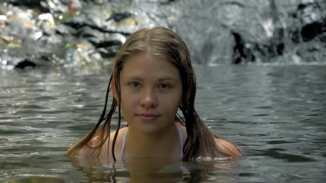 Portrait of beautiful woman bathing in pond in the forest with small waterfall on the background.