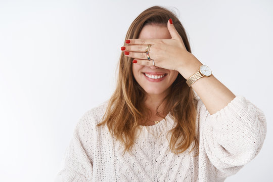 Charming caucasian girl hiding eyes behind palm smiling happily anticipating surprise playing hide-n-seek fooling around unable see close sight, standing positive joyful white background