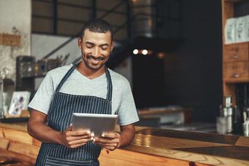 Smiling male cafe owner looking at digital tablet