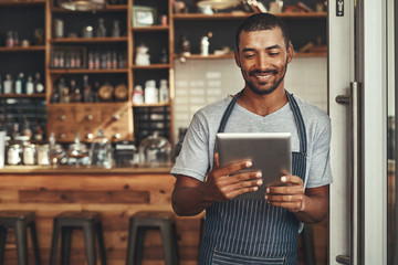 Young male cafe owner looking at digital tablet