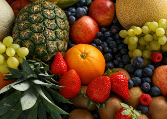 Variety of fresh fruits and berries on dark background: cantaloupe, melon, watermelon, blueberry, oranges, apple, strawberry, pineapple, mango, grapes and kiwi.