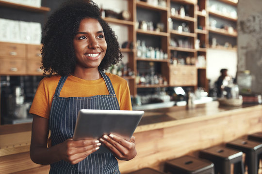 Young female owner holding digital tablet in her cafe looking aw