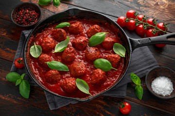 Homemade Meatballs in iron cast with sweet and hot tomato sauce, basil. On wooden table